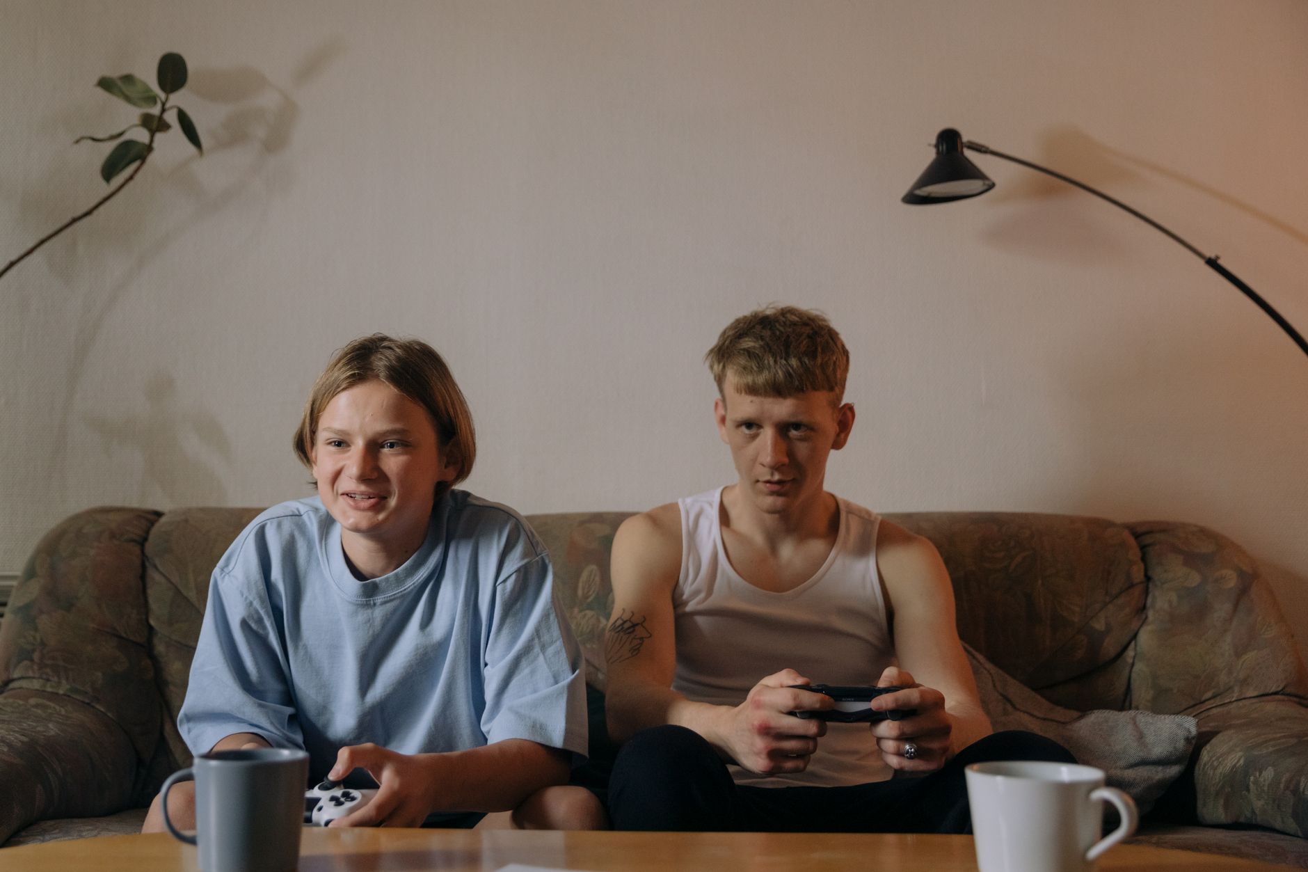 Two young men engaging in gaming on a sofa, enjoying a relaxed indoor setting.