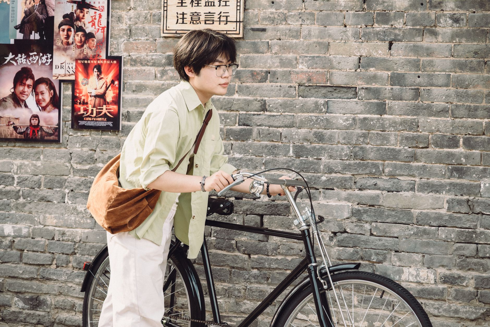 Young cyclist with urban style on a bike by a wall with vintage posters.