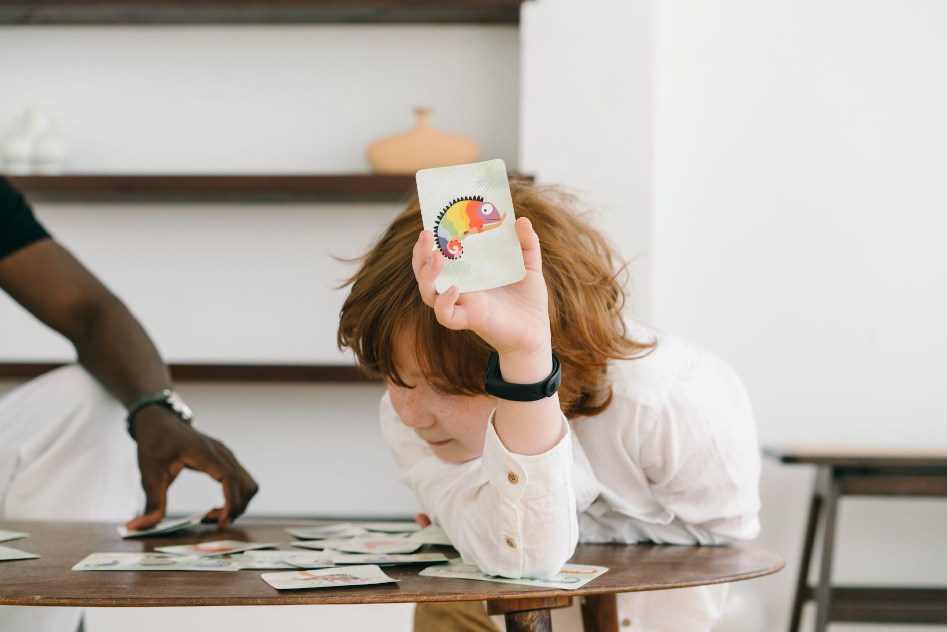 Child focused on a colorful chameleon flash card during an educational game indoors.