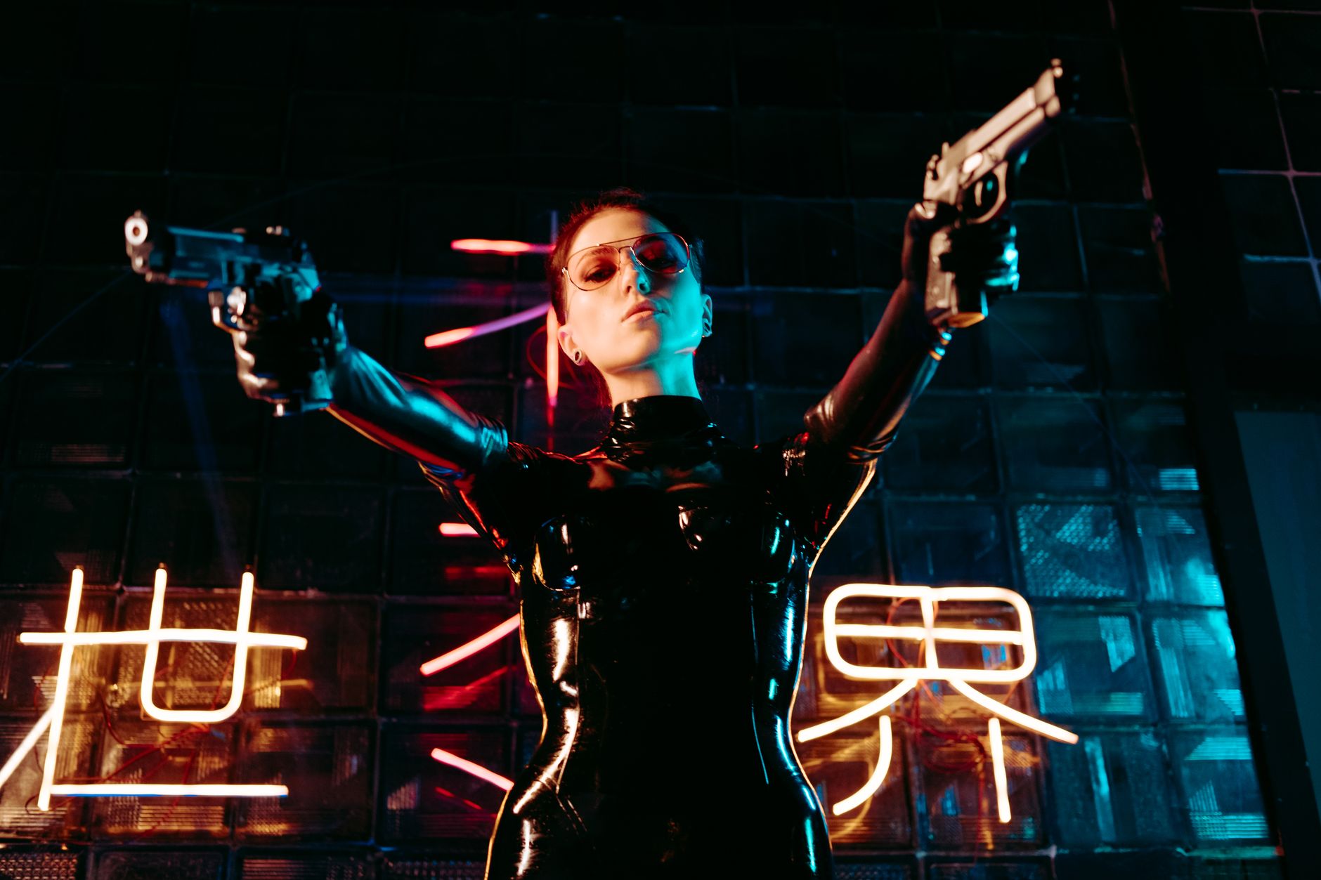 A performer in a sleek leather costume poses dramatically, holding guns under neon lights.