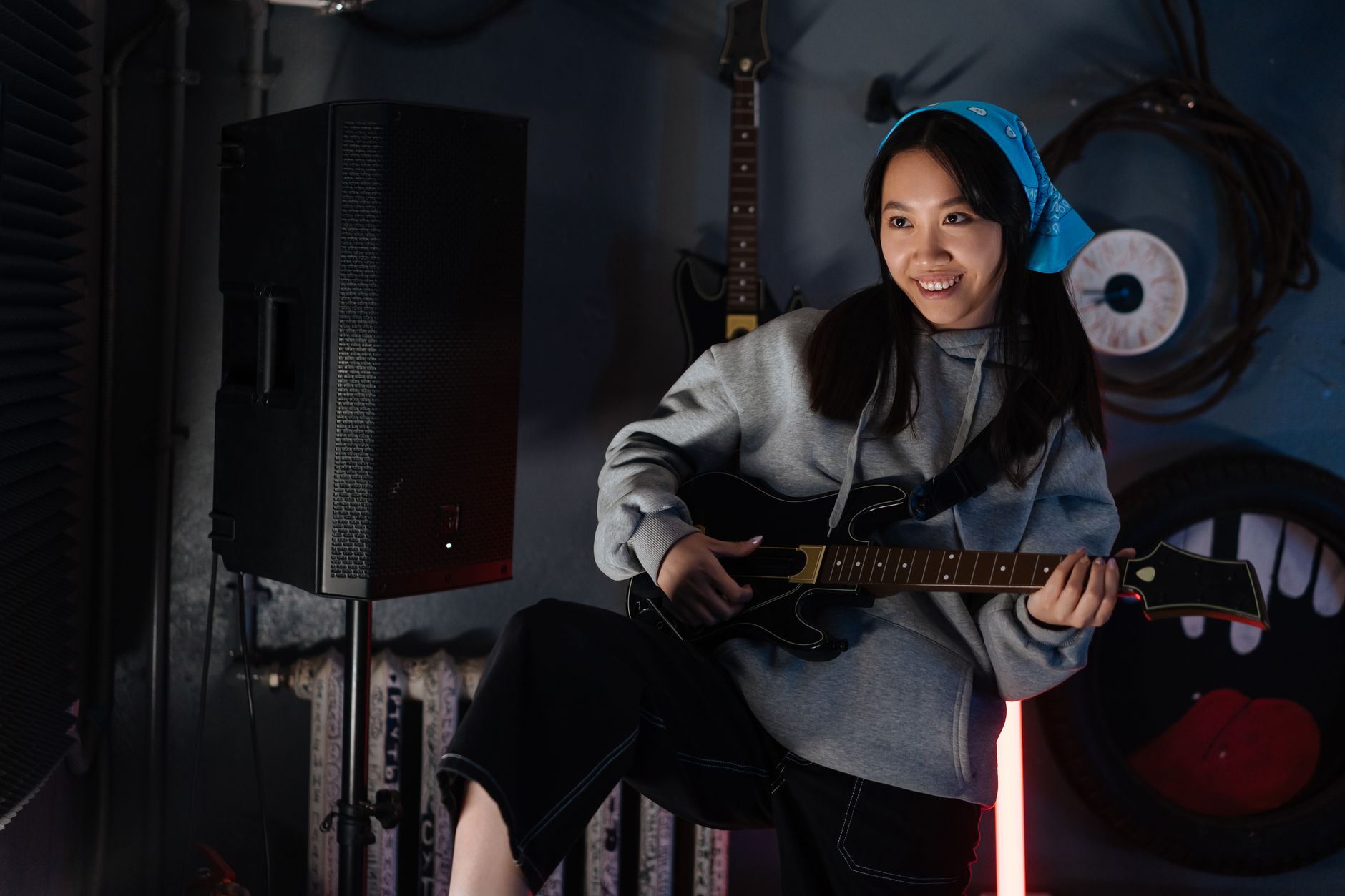 An enthusiastic young woman playing a video game with a guitar controller indoors, showcasing gaming joy.