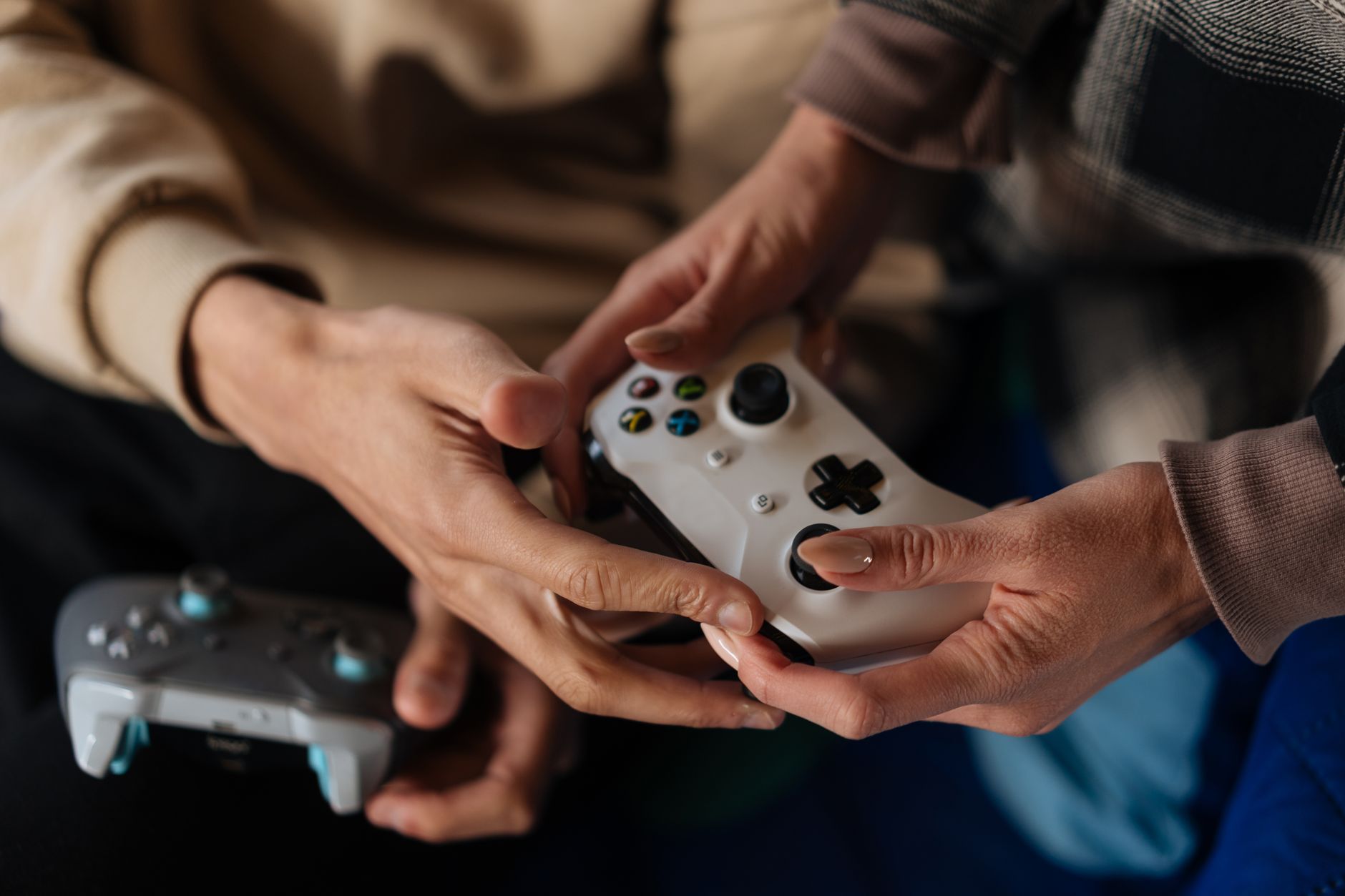 Close-up of two adults using game controllers for video gaming indoors.