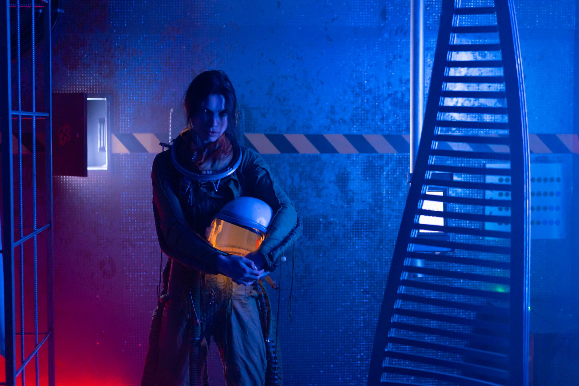 A female astronaut holding a helmet in a dramatic, futuristic setting with blue and red lighting.