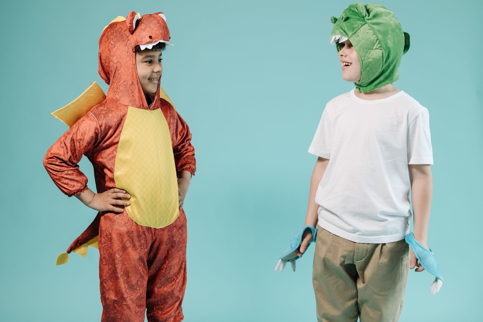 Two kids in dinosaur costumes joyfully pose against a turquoise background.