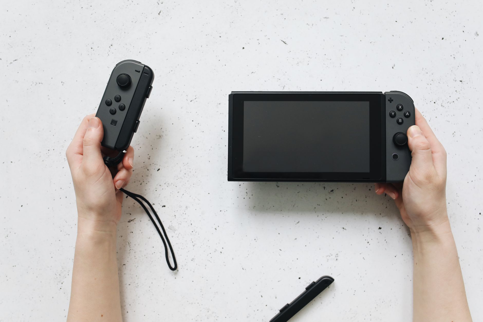 Close-up of hands holding a Nintendo Switch and Joy-Con controllers on a white surface.