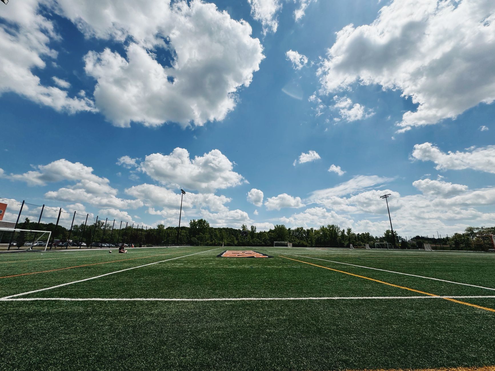 A vibrant outdoor soccer field under a blue sky with scattered clouds.