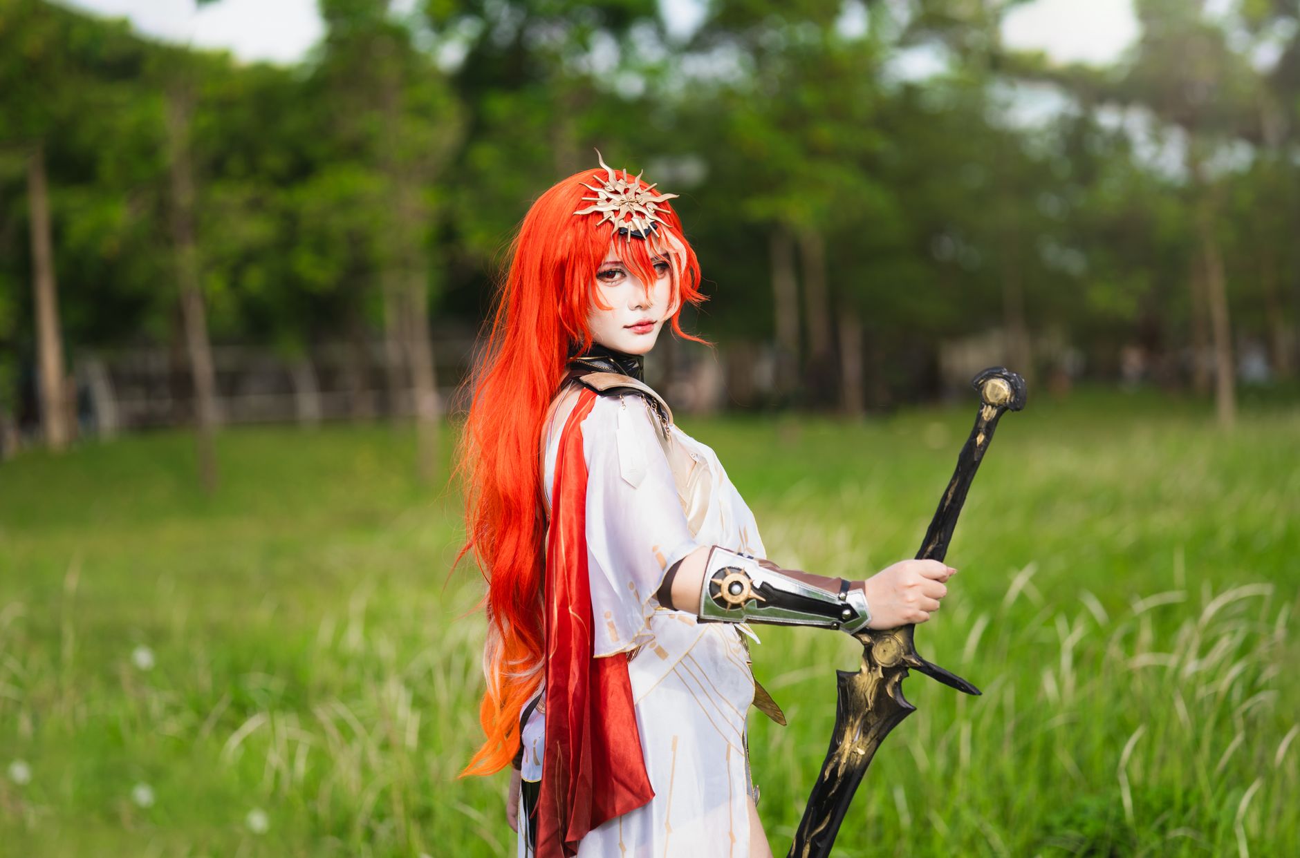 Striking cosplay of a fantasy warrior with red hair holding a sword in a vibrant grassy field.
