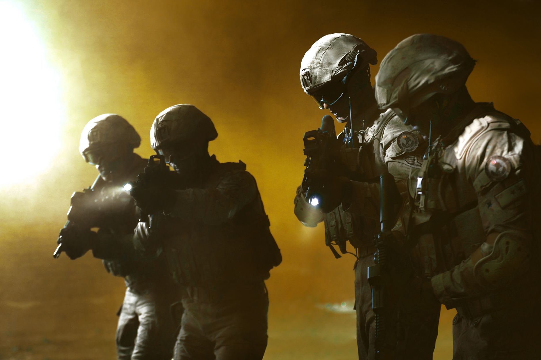 Four soldiers in tactical gear advancing in a smoky battlefield setting.