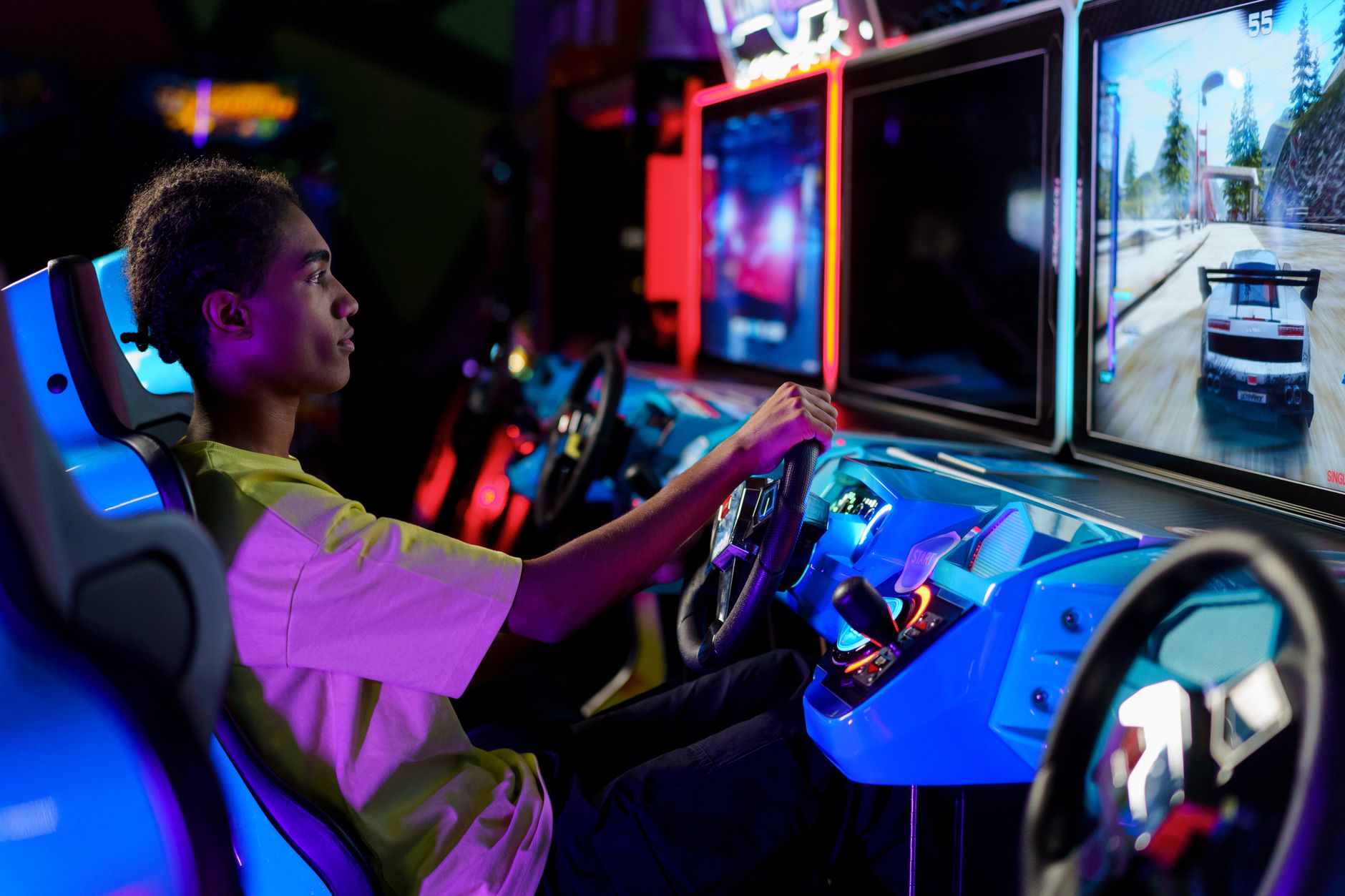 A young man intensely plays a car racing video game at an amusement arcade.