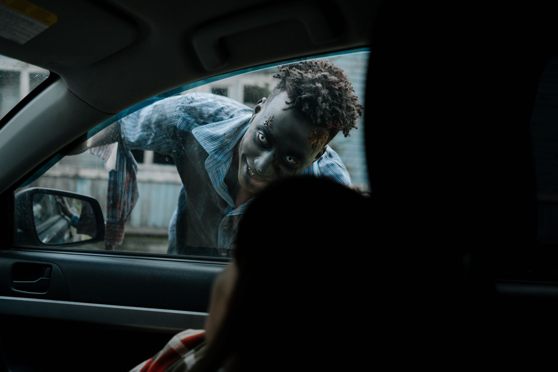 Frightening zombie peering through a car window during a horror scene.