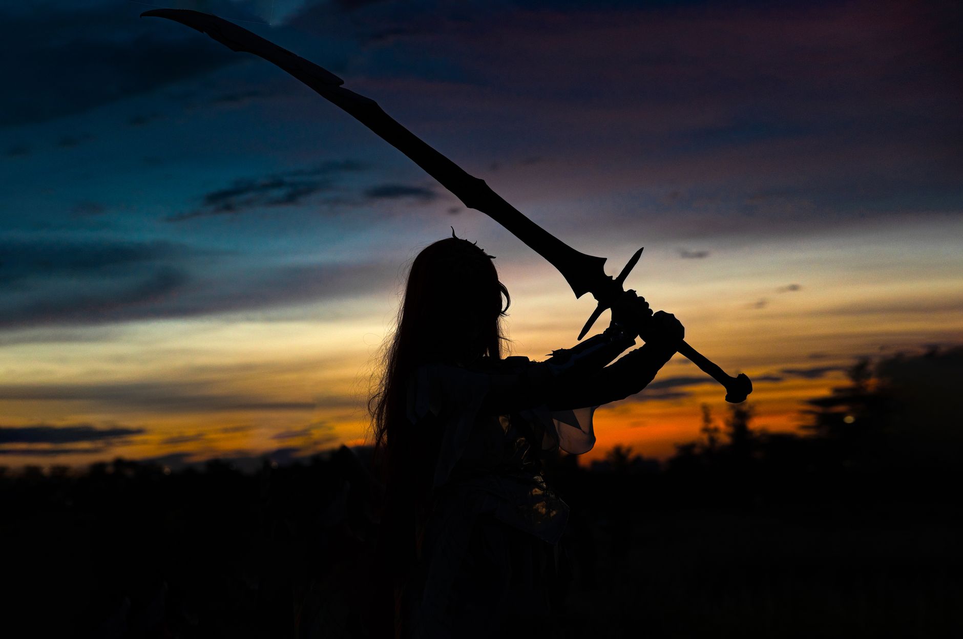 A dynamic silhouette of a cosplayer posing with a sword against a stunning sunset backdrop.