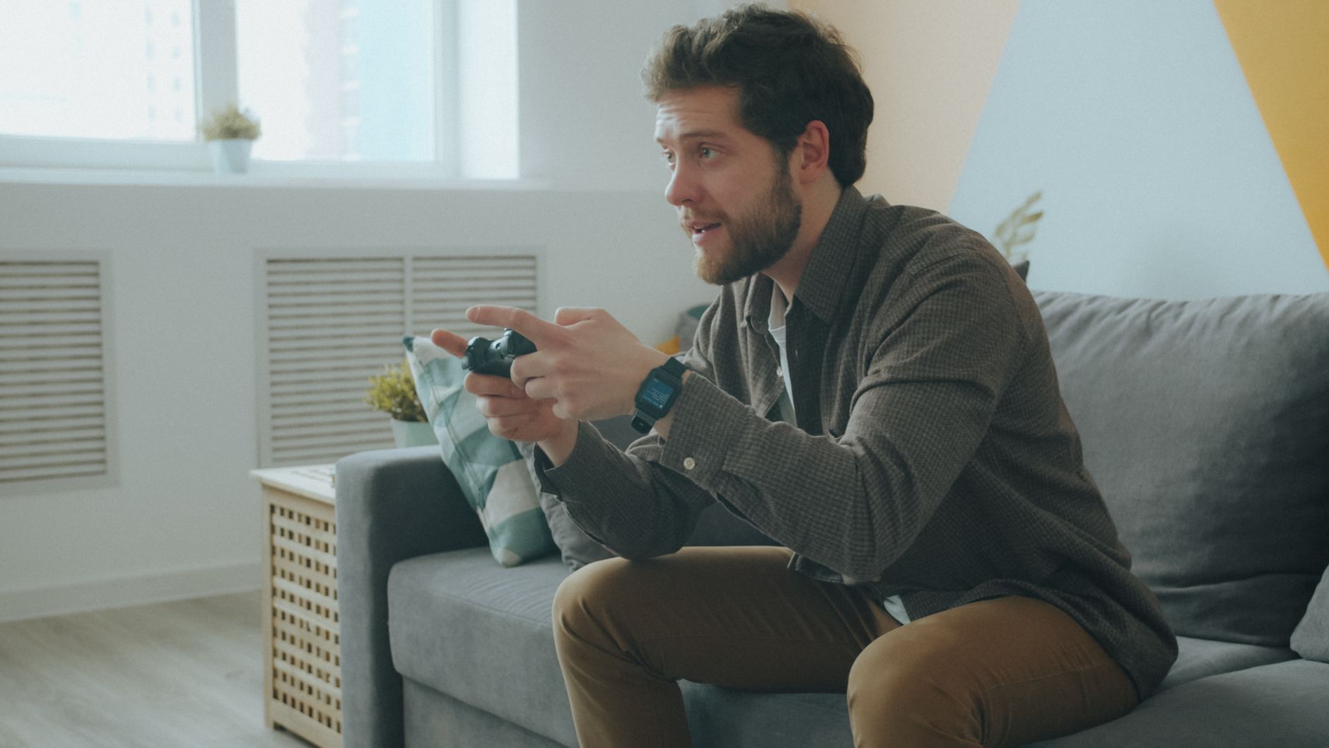 A man focused on playing video games on a console in a modern living room setting.