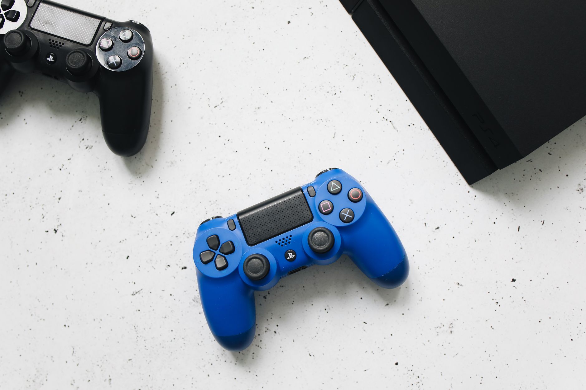 Blue and black PlayStation controllers with console on a white surface, minimalist style.