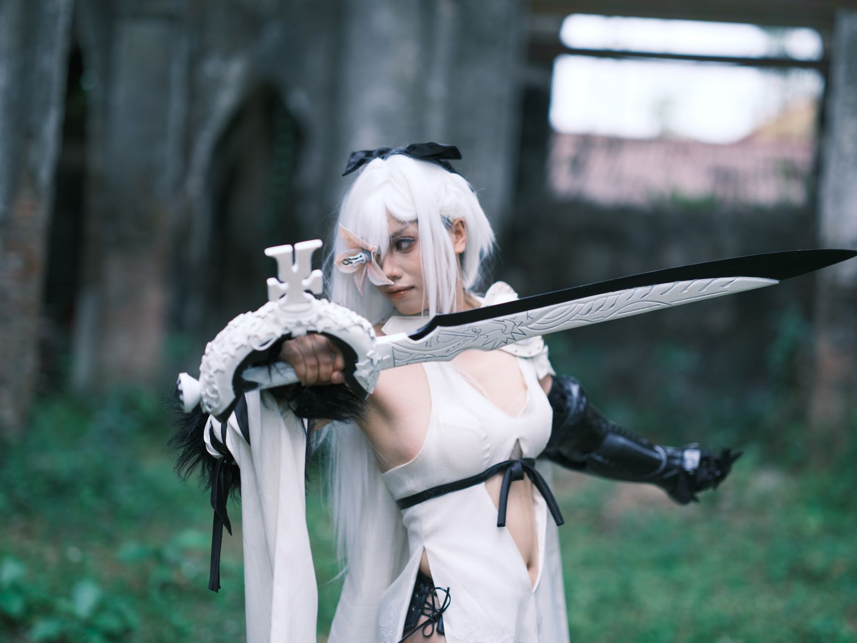 Cosplayer as a white-haired warrior with a sword poses outdoors in Việt Nam, showcasing intricate costume design.