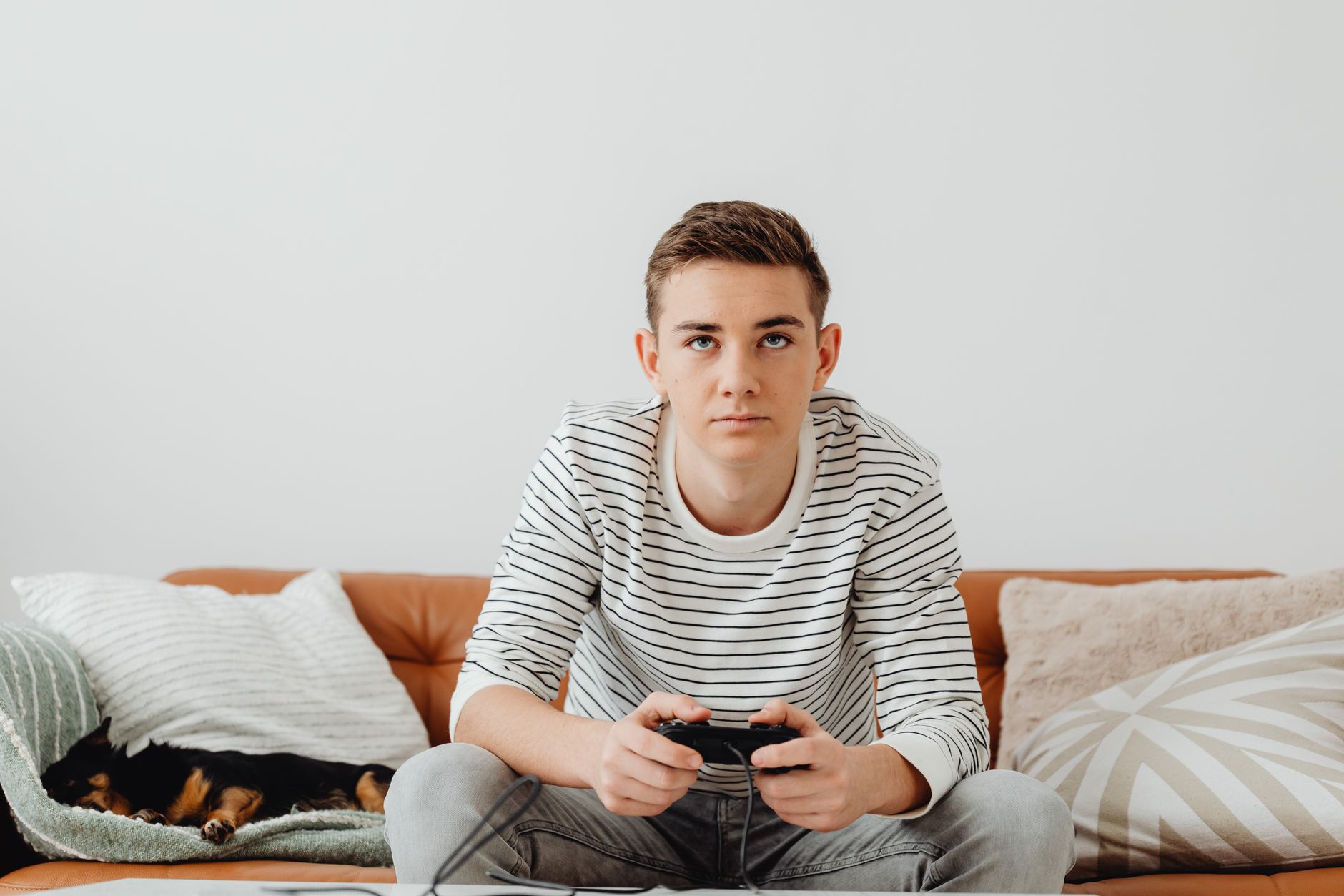 Teen boy intensely focused on video games at home, relaxing on a couch.