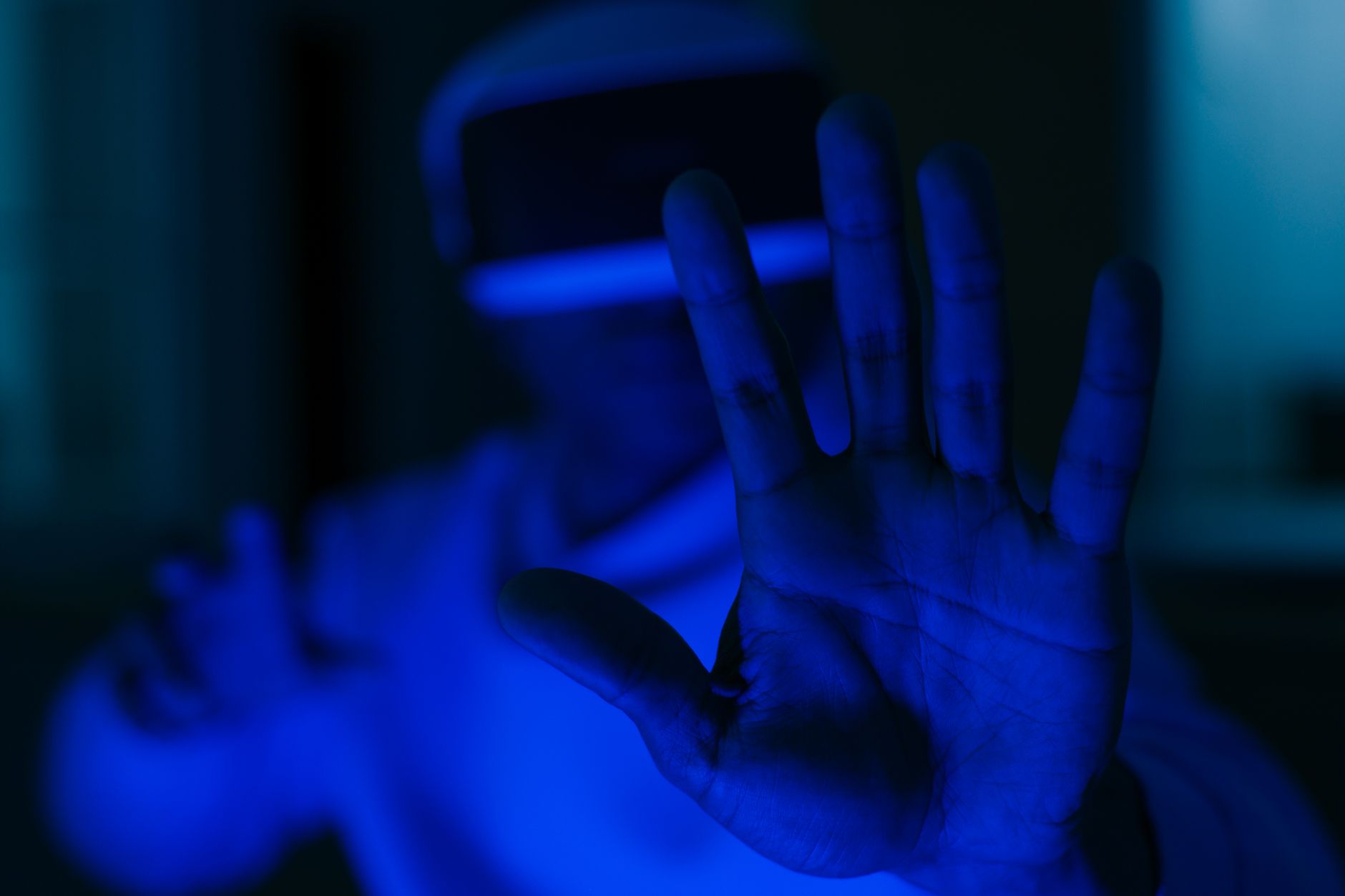 A person using VR glasses with outstretched hands in a futuristic blue-lit environment.
