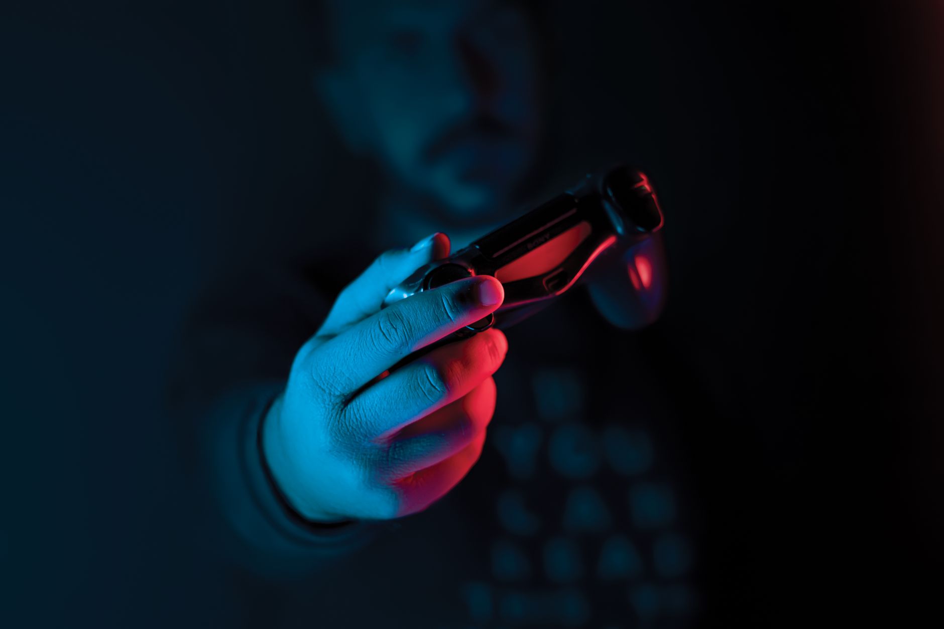 Close-up of a man's hand holding a joystick against a dark background with red and blue lighting.