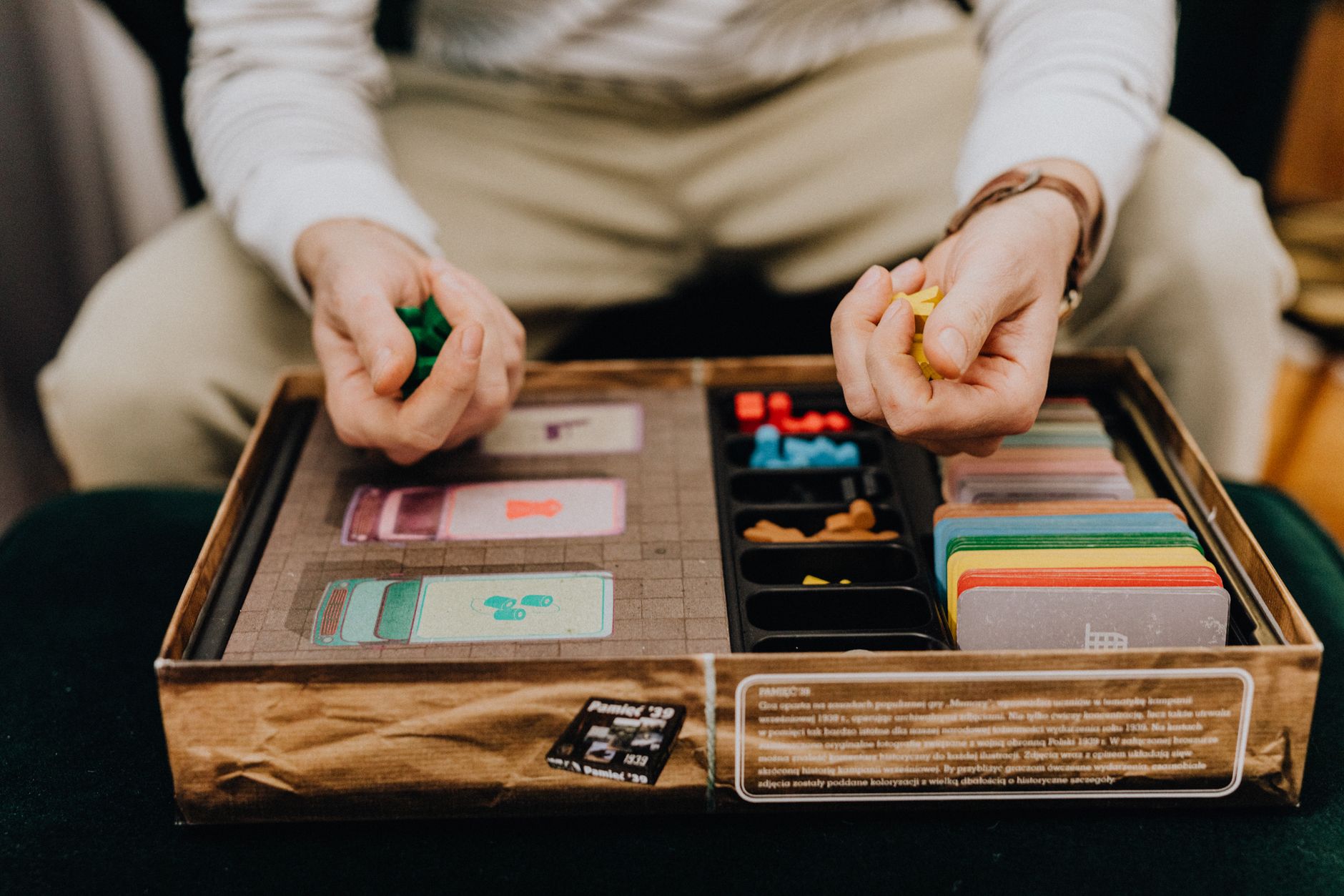 Person playing a board game with colorful pieces and cards indoors, focused and engaging.