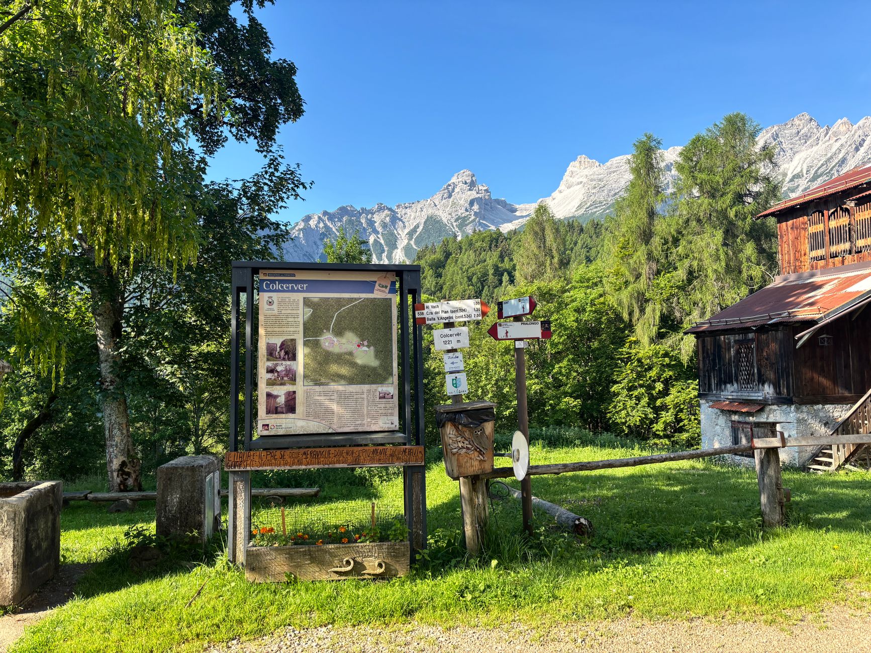 Information board and signs in a mountain village with scenic alpine background.