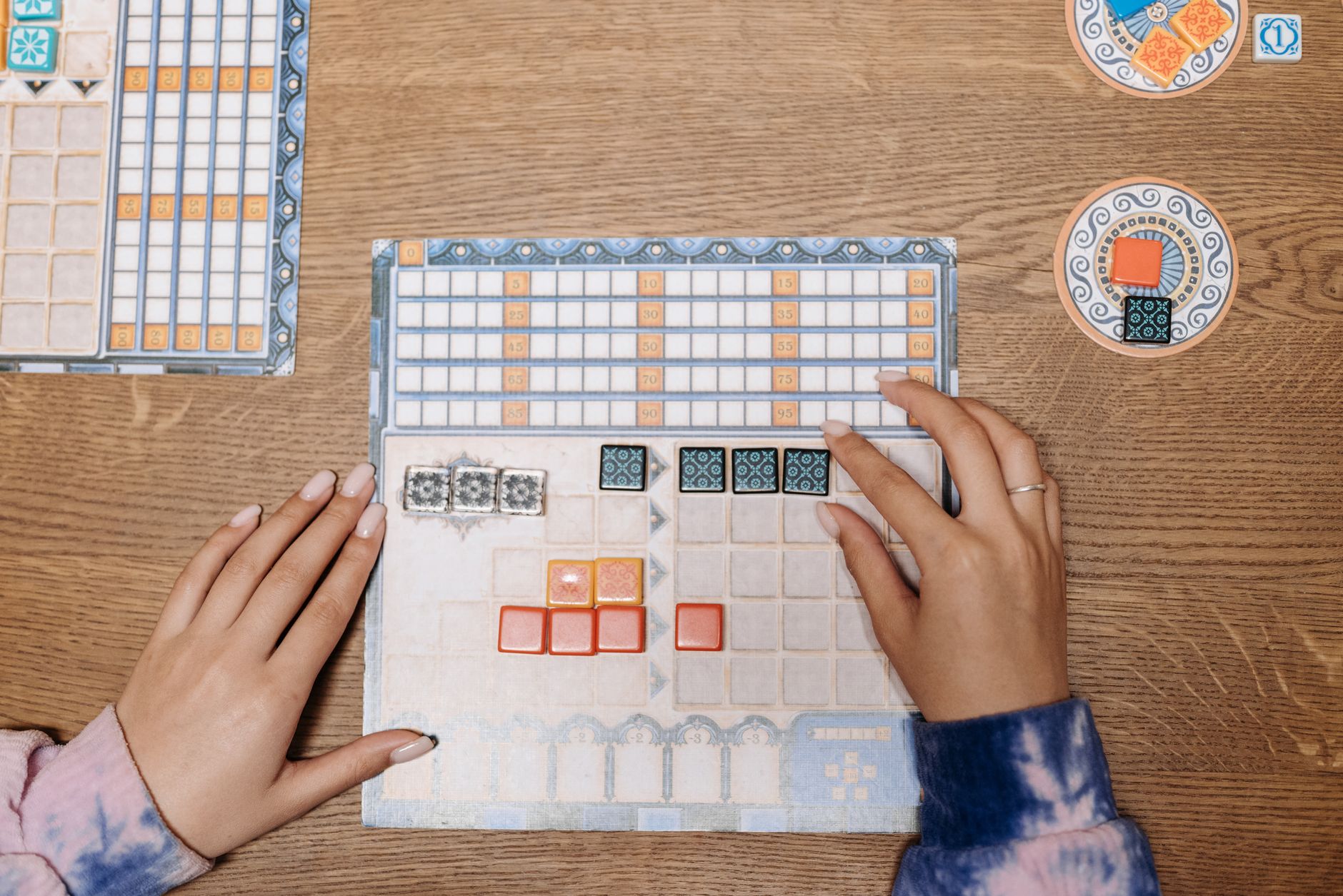 Hands arranging tiles on a strategic board game during a fun game night.